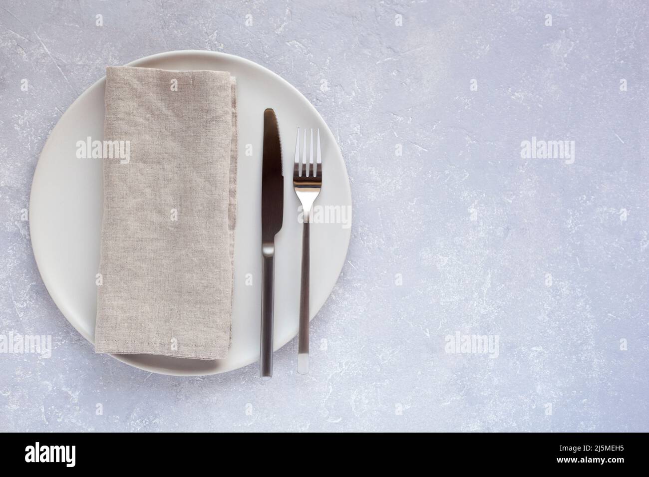 piatto tondo bianco con posate e tovagliolo di lino su fondo di cemento grigio chiaro, stile minimalismo, vista dall'alto, spazio copia, Foto Stock