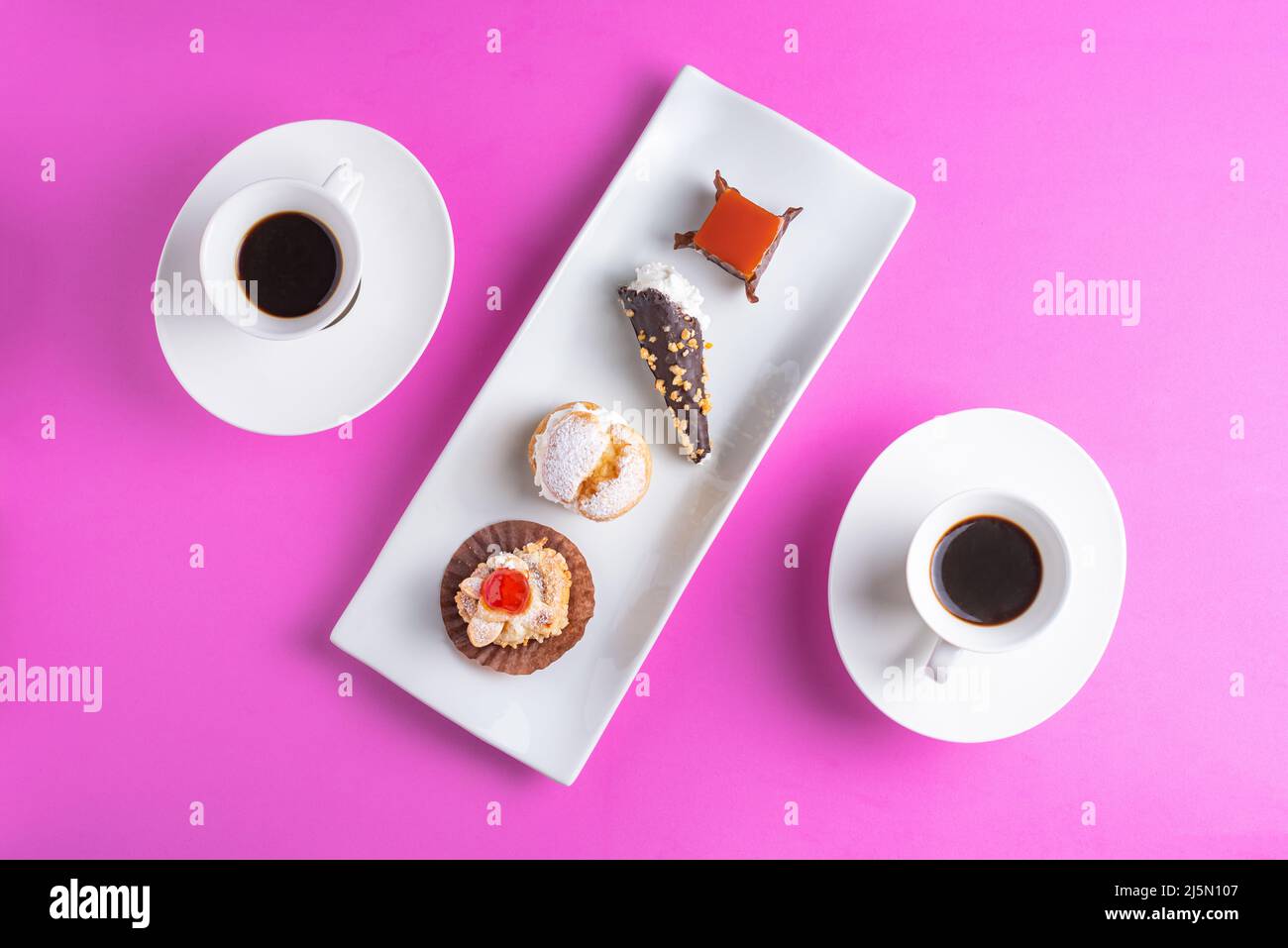 Diverse torte su un piatto rettangolare bianco con una tazza di caffè su ciascun lato formando una figura diagonale. Foto Stock