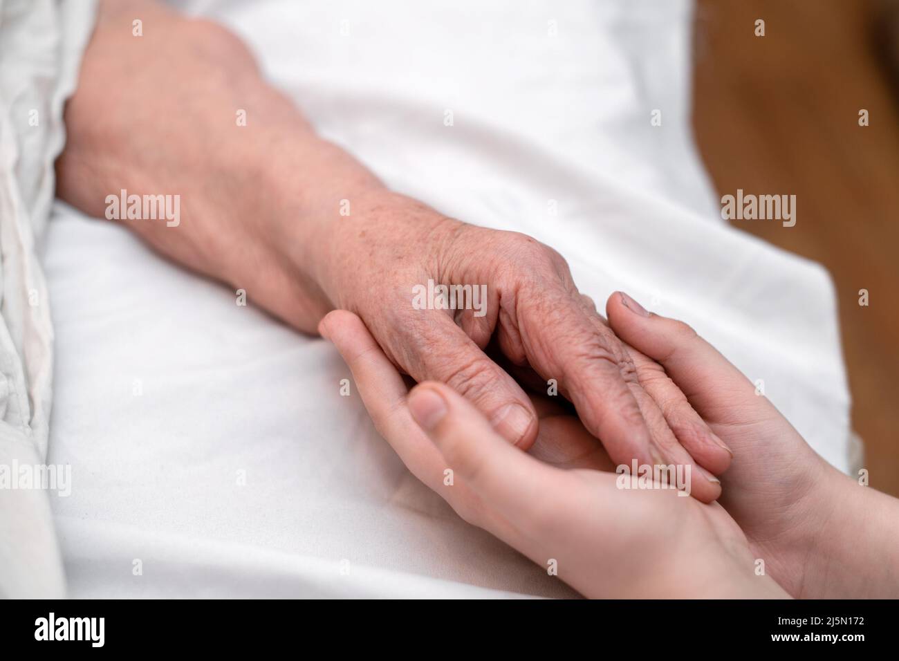 Le mani del nipote tengono la mano rugosa di una nonna anziana malata in una clinica medica. Il concetto di amore e cura. Movimento lento. Foto Stock