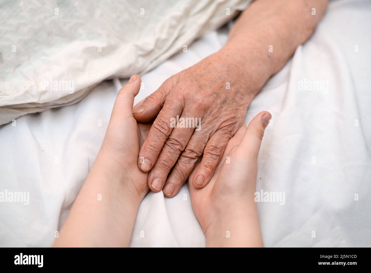 Le mani del nipote tengono la mano rugosa di una nonna anziana malata in una clinica medica. Il concetto di amore e cura. Movimento lento. Foto Stock