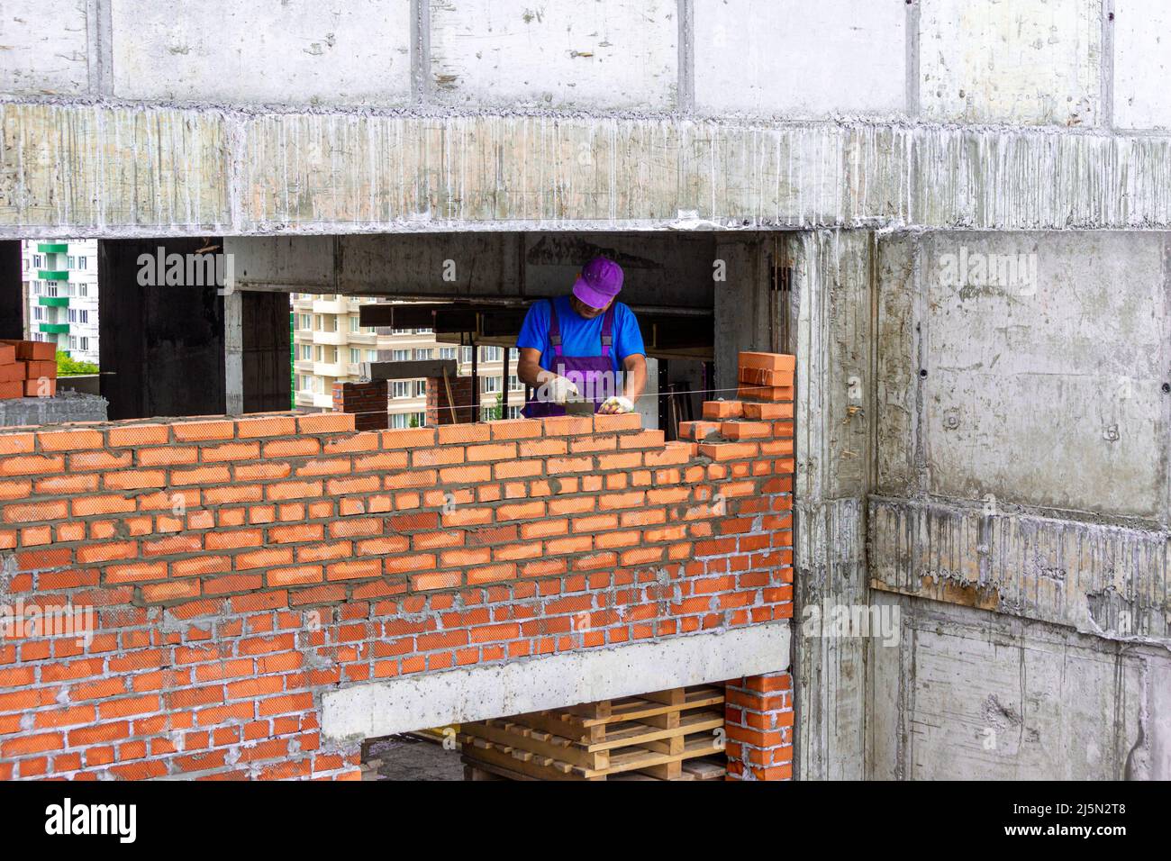 Bricklayer stende una partizione durante la costruzione di una struttura monolitica di telaio, fuoco selettivo Foto Stock