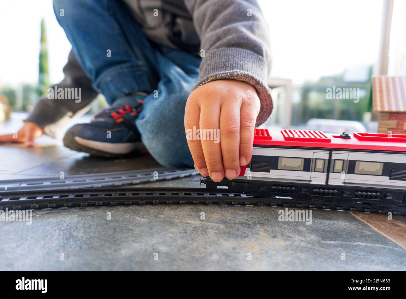 VYoung bambino che gioca con i treni giocattolo sul pavimento. Treno giocattolo simile al treno spagnolo Cercanias Renfe e al treno ad alta velocità Ave Foto Stock