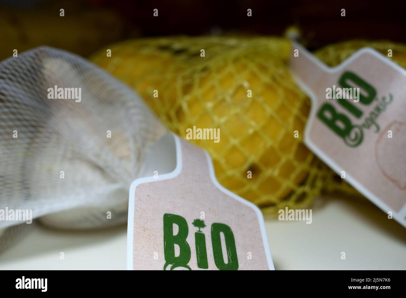 Aglio biologico biologico biologico e limoni gialli in una rete di frutta con un'etichetta indicante il prodotto biologico sulla tavola con banane sullo sfondo Foto Stock
