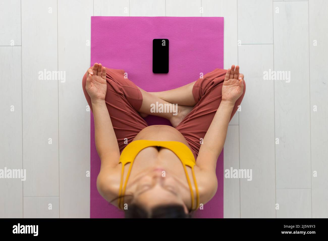 Donna incinta meditating a casa attendendo bambino che fa il codice prenatale in linea yoga la classe che si sieta in posizione del loto, esercitandosi nella meditazione per mentale sano Foto Stock