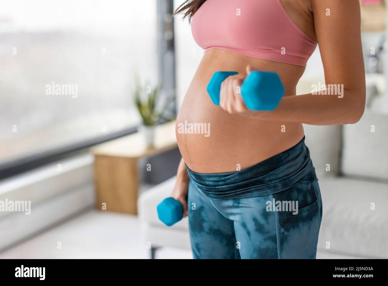 Donna incinta esercizio di allenamento di forza fitness con manubri a casa. Pesi del corpo braccio di allenamento riccioli primo piano della pancia Foto Stock
