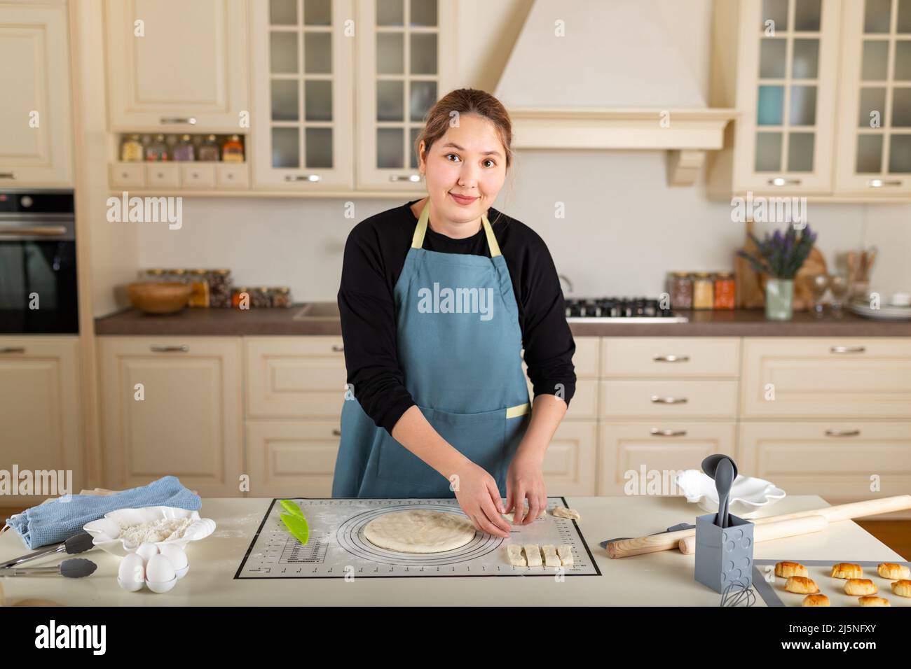 La giovane donna kazaka sta cucinando la cottura all'interno di una moderna cucina casalinga. Foto Stock