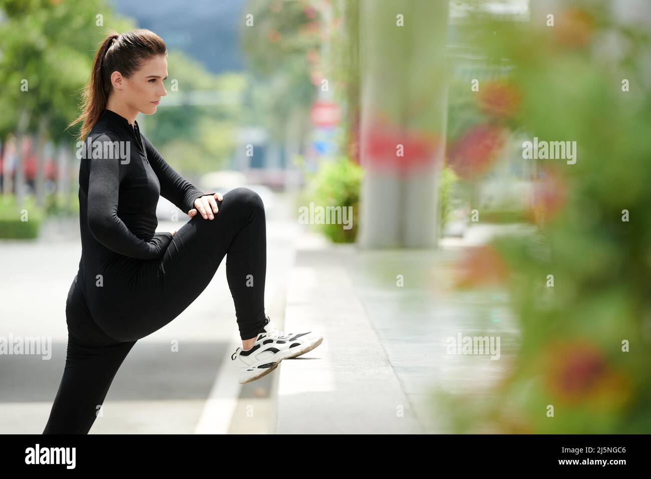 Determinato sportivo giovane allungando le gambe dopo la corsa per mantenere i muscoli suppli ed impedire loro di accorciarsi Foto Stock