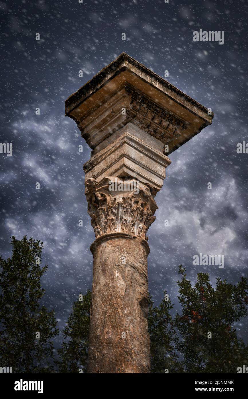 Nevicate nell'antica colonna corinzia contro il cielo tempestoso al Foro Romano di Roma. La colonna si trova accanto al Tempio di Romolo. Foto Stock