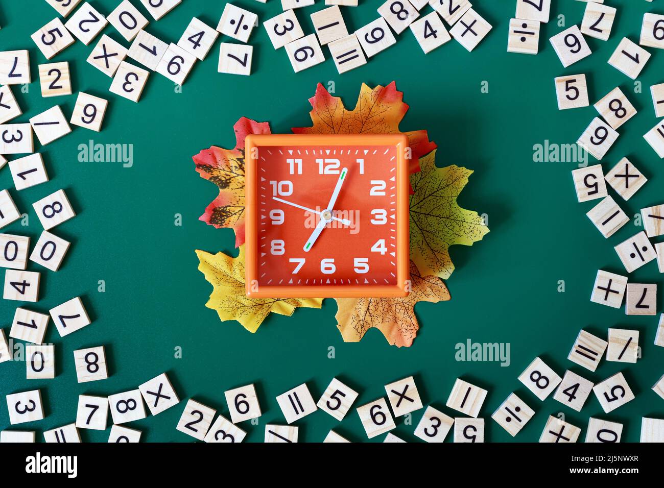 Sveglia arancione che mostra 7 am circondato da numeri di matematica su sfondo verde. Concetto di ritorno a scuola. Disposizione piatta. Foto Stock