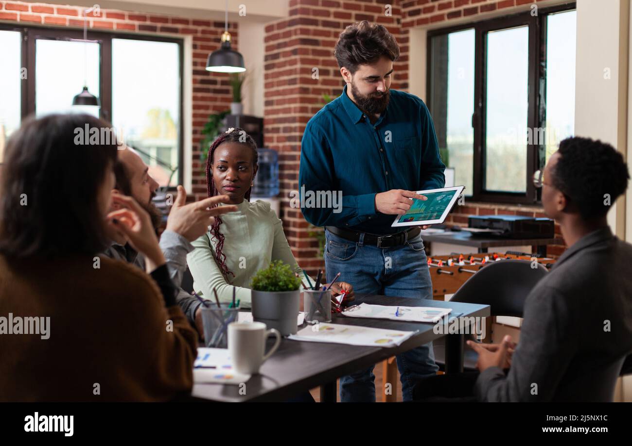 Uomo d'affari che presenta il fatturato dell'azienda durante l'incontro d'affari nell'ufficio di startup che lavora alla strategia di vendita. Imprenditori multietnici brainstorming idee per il progetto di gestione Foto Stock