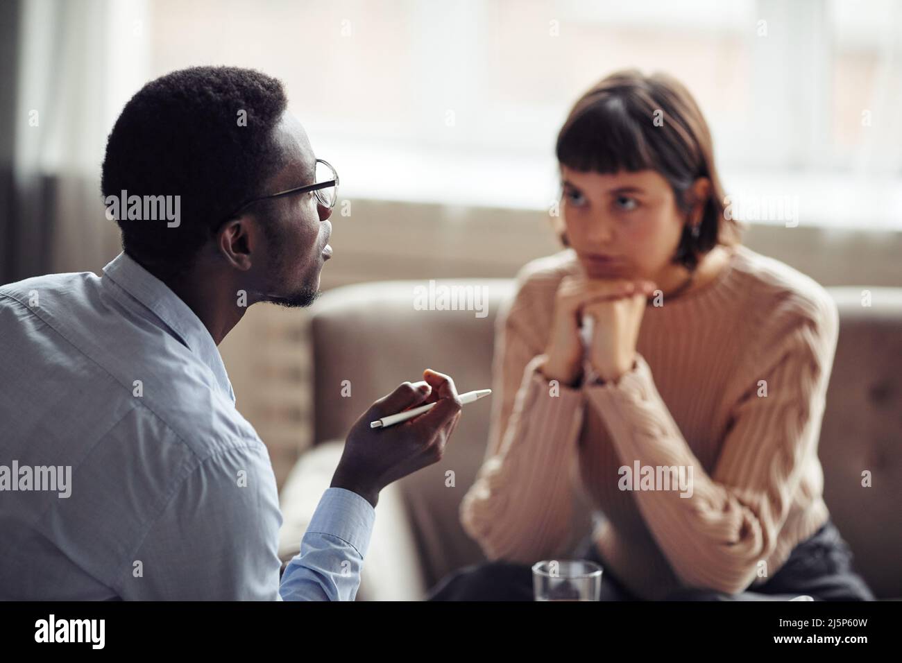 Consigliere afroamericano con penna in mano che spiega qualcosa al paziente durante la conversazione Foto Stock