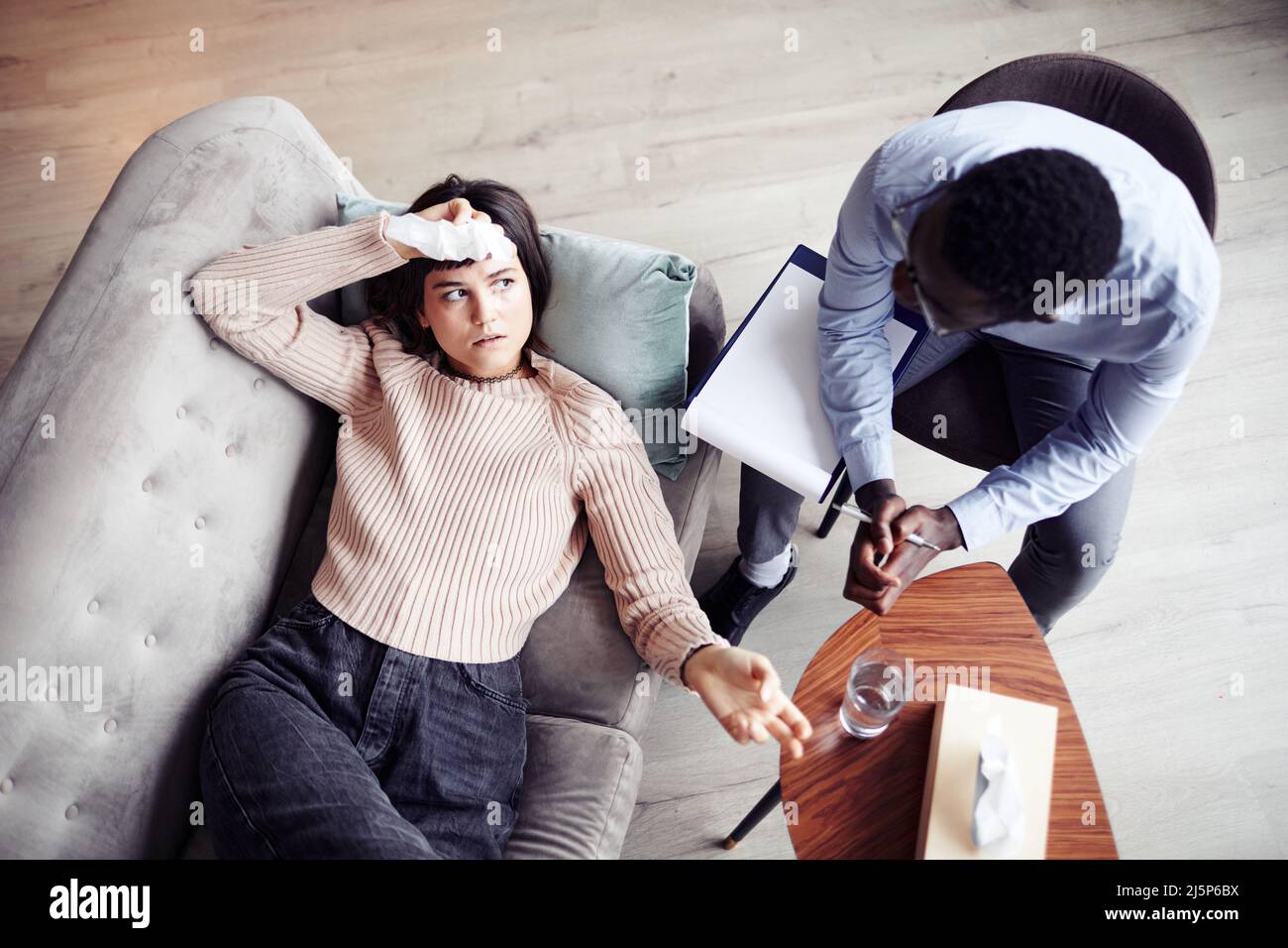 Giovane donna emozionale sdraiata sul divano durante la sessione di psicoterapia e condividendo pensieri con il terapeuta Foto Stock