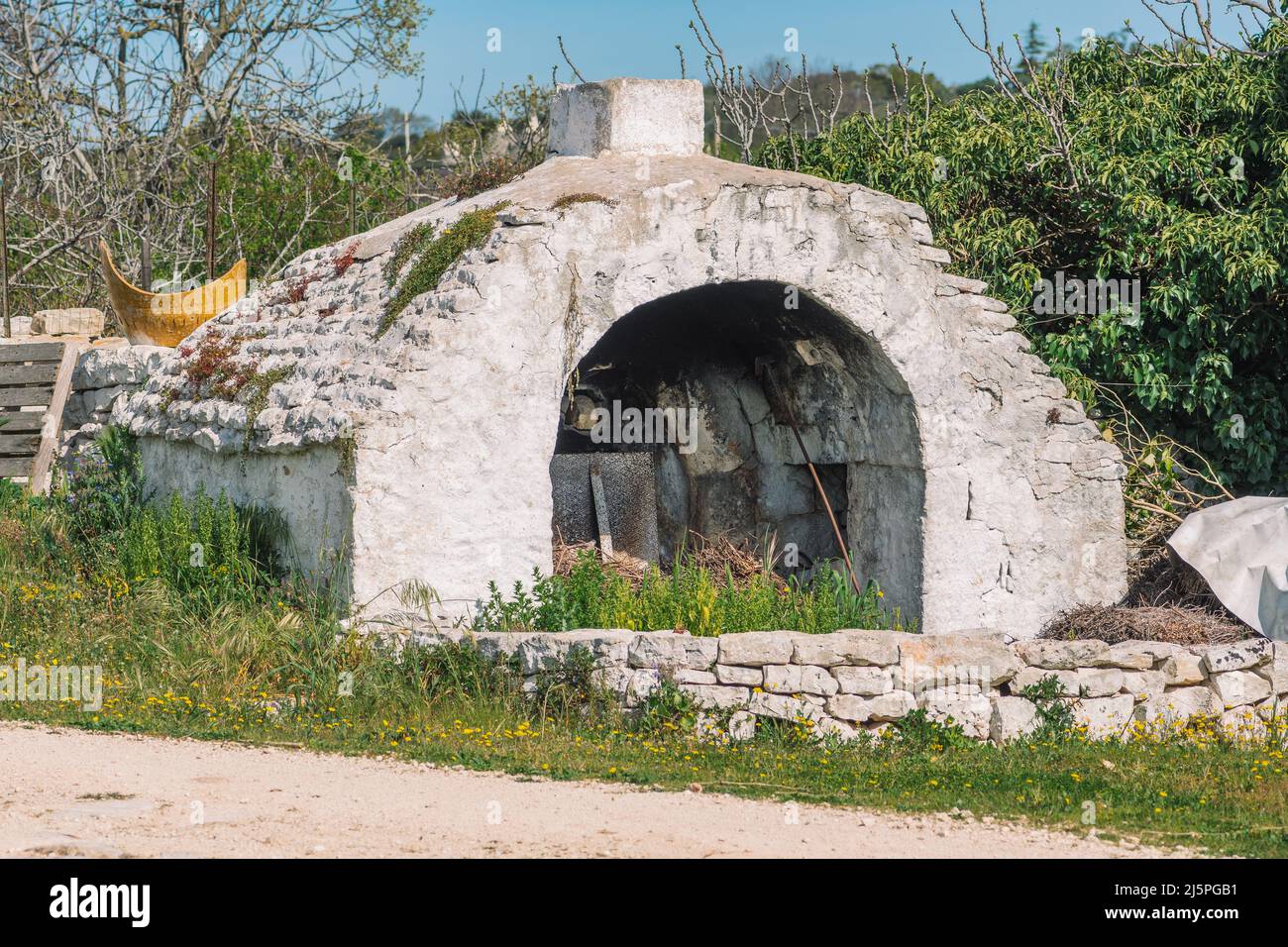 Bel forno o camino in pietra bianca tradizionale nella campagna pugliese, Italia con pareti in pietra asciutta e natura circostante Foto Stock