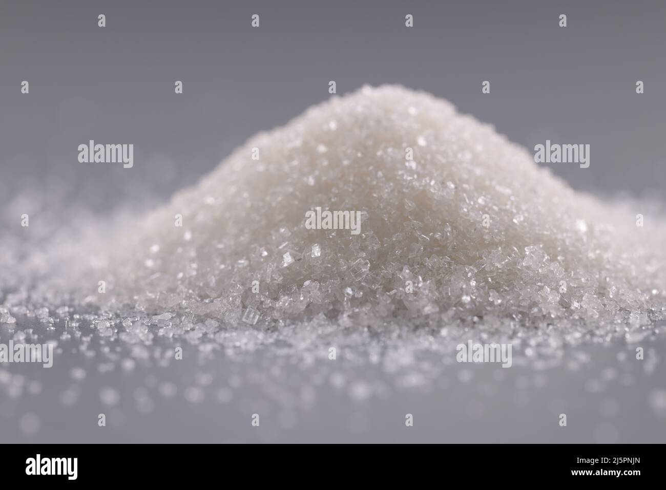 Mucchio di cristalli di zucchero sulla superficie grigia, mucchio di polvere dolce da aggiungere in piatti Foto Stock