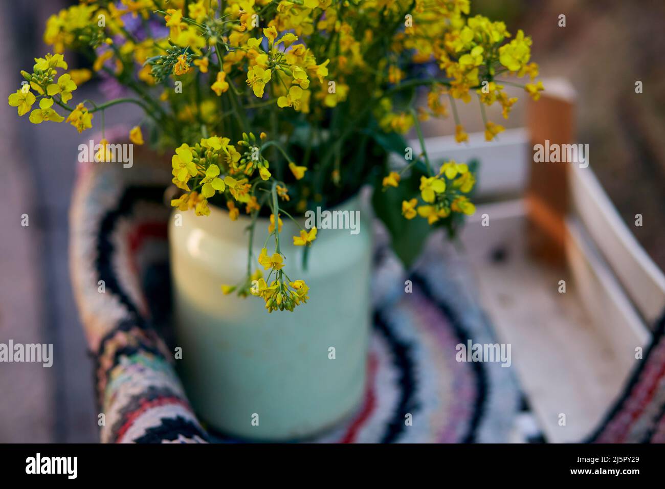 Naturale vintage colorato tappeto fatto a mano e fiori di primavera in annaffiatoio. Vita di paese, nucleo del cottage, concetto rustico creativo di patchwork Foto Stock