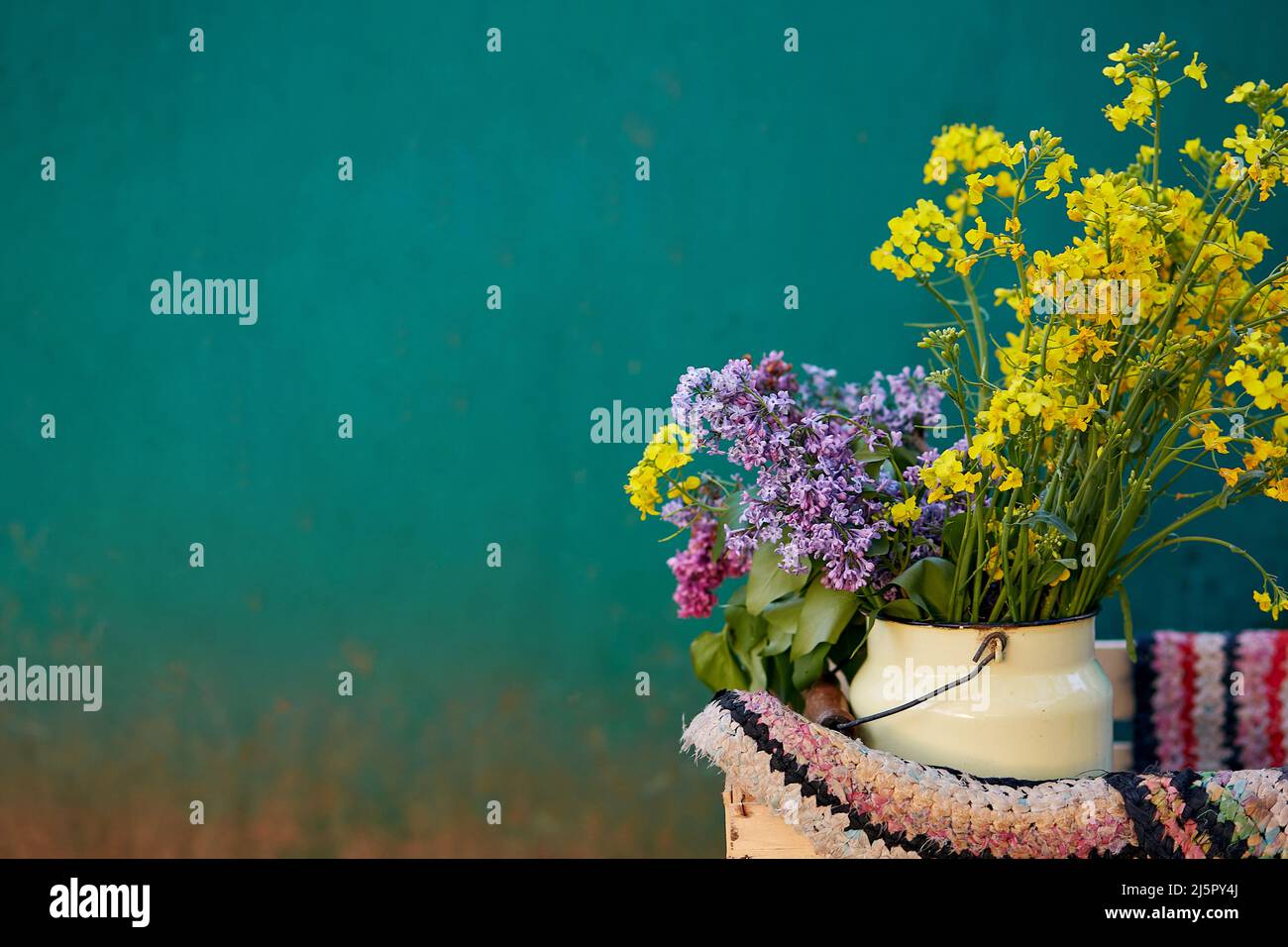 Annaffiatoio giallo vintage colorato con tappeto fatto a mano. La vita di paese, nucleo di cottage, concetto rustico creativo di patchwork. Spazio di copia. Foto Stock