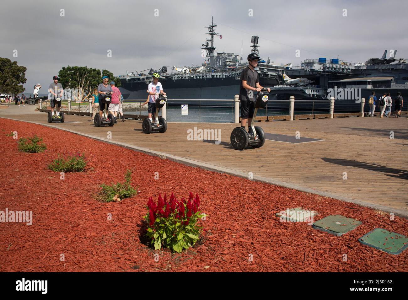 Gruppo di turisti che cavalcano segway di fronte alla portaerei USS Midway, il Molo della Marina di San Diego Foto Stock