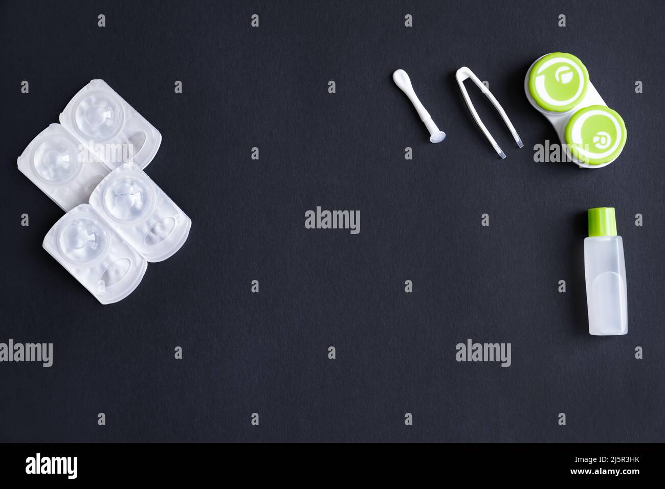 Lenti a contatto, contenitore, pinzette, ventosa e bottiglia con soluzione su sfondo nero, vista dall'alto, spazio di copia Foto Stock