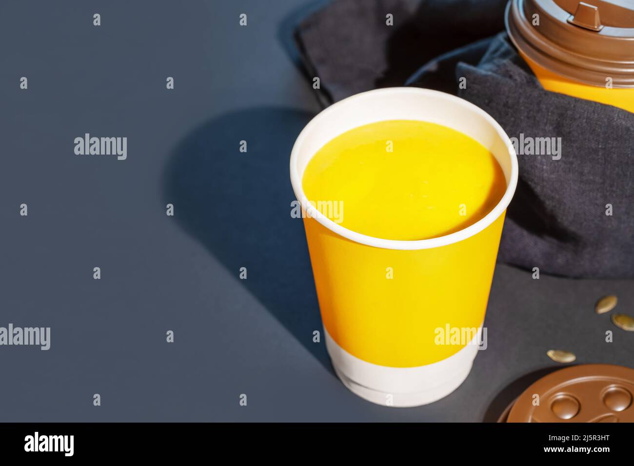 Zuppa di crema di zucca vegana spessa con semi in tazza monouso su sfondo blu scuro con spazio copia. Concetto di zuppa per andare, togliere cibo e healt Foto Stock