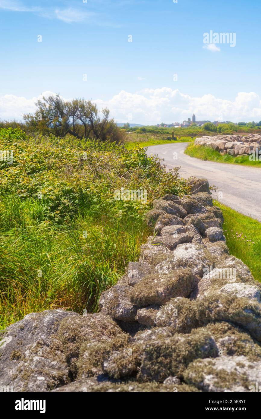 Mura asciutte che costeggiano la strada rurale in Normandia, città in foschia all'orizzonte Foto Stock