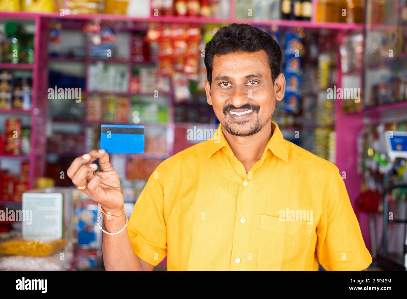 Sorridendo kirana o commerciante di drogheria che mostra la carta di credito guardando la macchina fotografica al negozio di alimentari - concetto di pagamento della carta di credito, shopping e piccolo Foto Stock