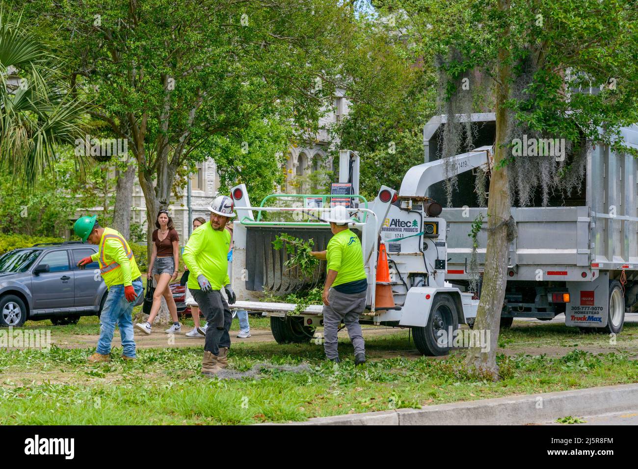 NEW ORLEANS, LA, Stati Uniti d'America - 18 APRILE 2022: Lavoratori che utilizzano il legno per sminuzzare filiali in St. Charles Avenue con studenti di passaggio in background Foto Stock