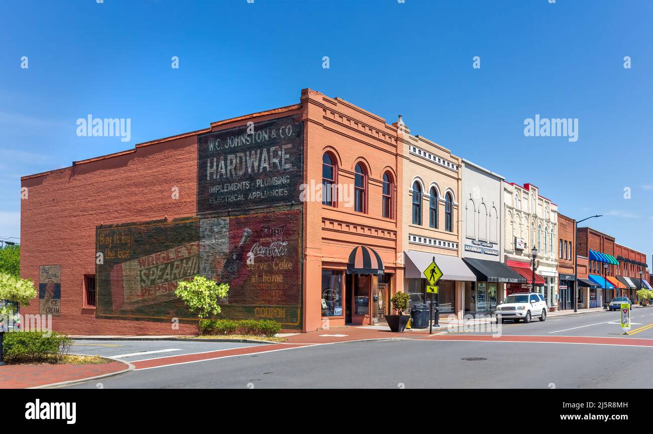 MOORESVILLE, NC, USA-17 APRILE 2022: Vista iconica di un blocco di edifici storici del centro, con la vecchia pubblicità dipinta sul muro terminale. Soleggiato, primavera, bl Foto Stock