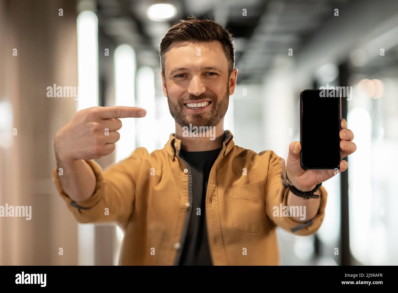 Uomo d'affari che punta allo schermo del telefono che si levano in piedi nella porta in ufficio Foto Stock