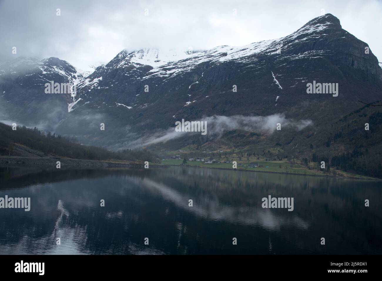 Coperto da folte nuvole in tempo nebbioso lago Oldenvatnet offre una vista mistica al villaggio Olden in Norvegia. Tiefhängenden Wolken mit Nebelschwad Foto Stock