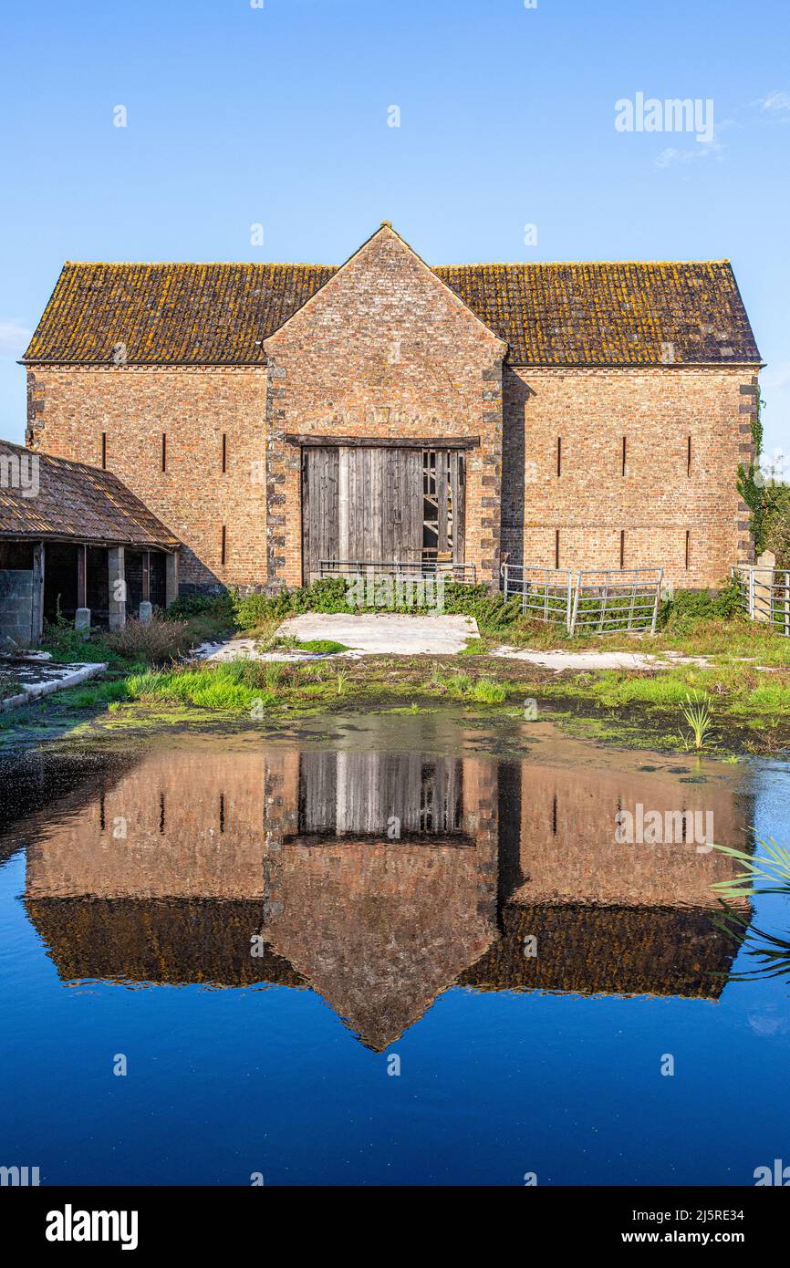 Un vecchio fienile di mattoni visto riflesso in una grande pozzanghera nel villaggio di Severnside di Arlingham, Gloucestershire, Inghilterra Regno Unito Foto Stock