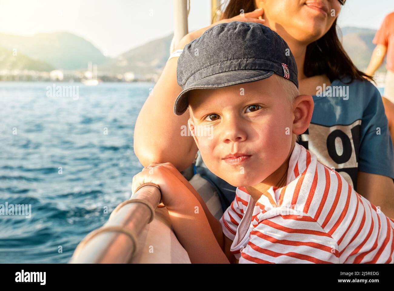 Il bambino simpatico con la madre gode di una gita in barca a vela in mare, passando per la costa di Marmaris. Ritratto di ragazzo in cappellino di protezione del sole in vacanza in Turchia primo piano Foto Stock