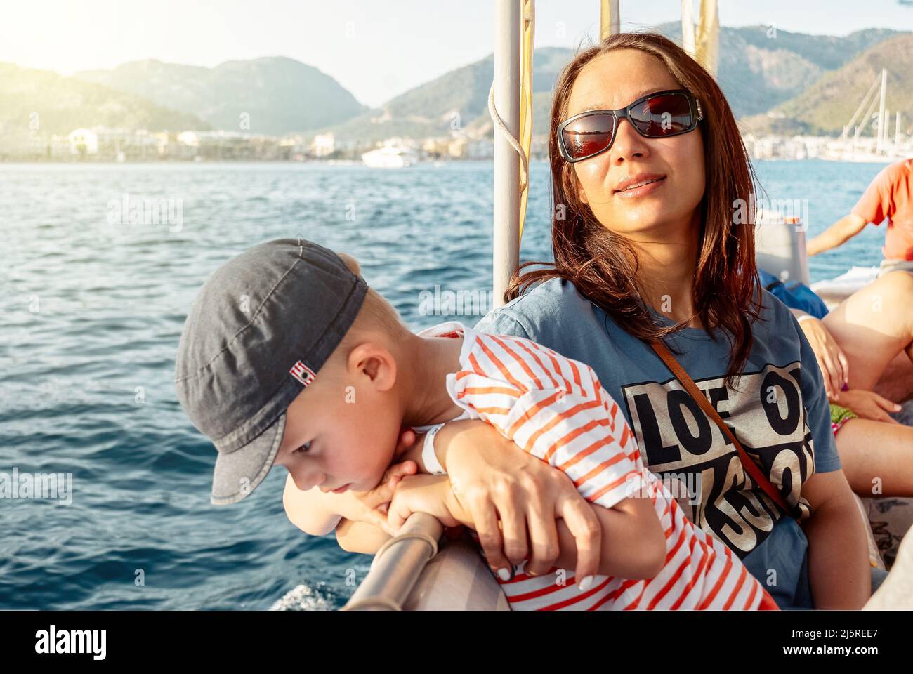 Madre e figlio si godono la vela in barca lungo la costa di Marmaris. Donna in occhiali da sole e simpatico bambino in cappello in vacanza estiva in Turchia vicino vista Foto Stock