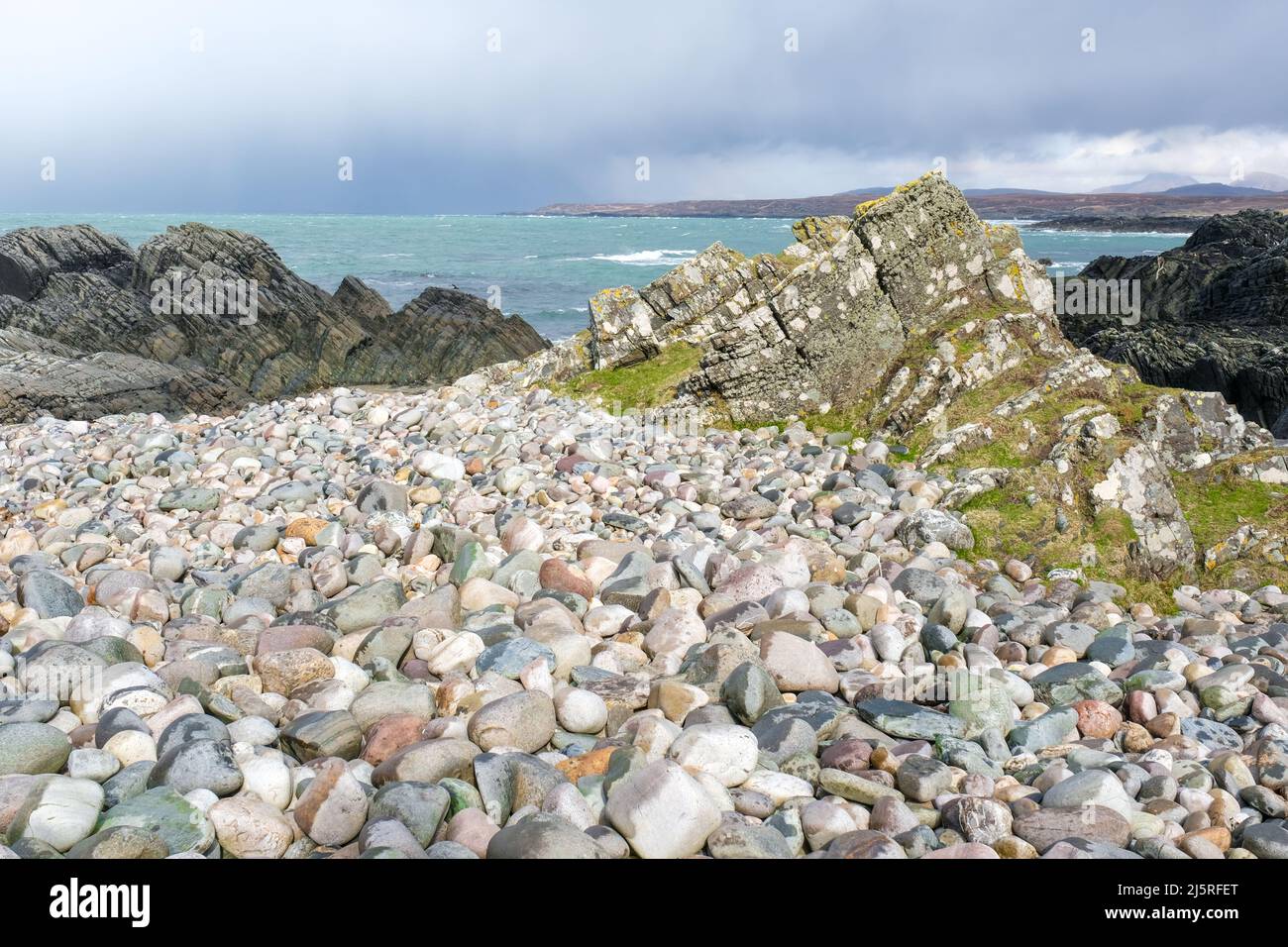Una vista costiera della remota baia di Sanaigmore, Islay con un primo piano di ciottoli colorati e i pap di Jura in lontananza. Foto Stock Una vista costiera della remota baia di Sanaigmore, Islay con un primo piano di ciottoli colorati e i pap di Jura in lontananza. Foto Stock