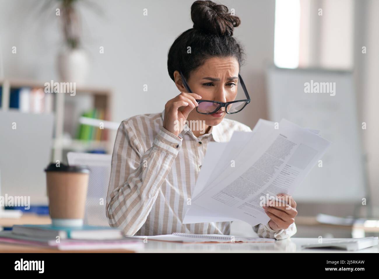 Responsabile dell'ufficio femminile che indossa occhiali e che fa i documenti, ha problemi di vista, seduto sul posto di lavoro Foto Stock