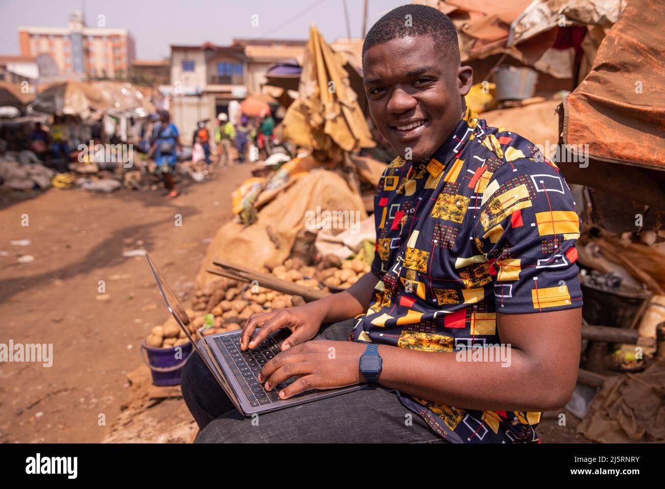 Il giovane ragazzo africano usa il suo computer sul mercato, i giovani e la tecnologia in africa Foto Stock