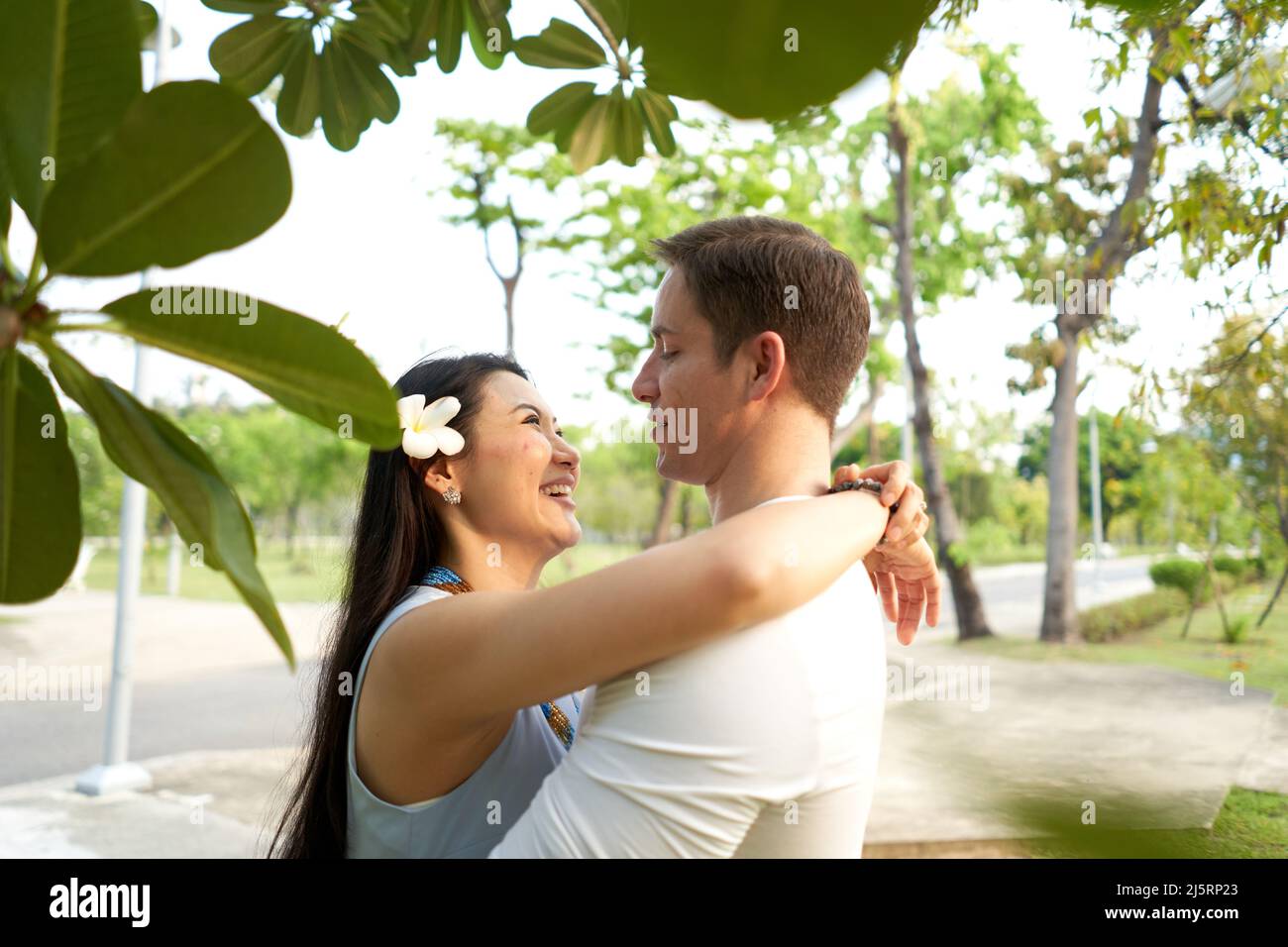Donna con un fiore tropicale bianco nei capelli che abbraccia un uomo in un parco Foto Stock