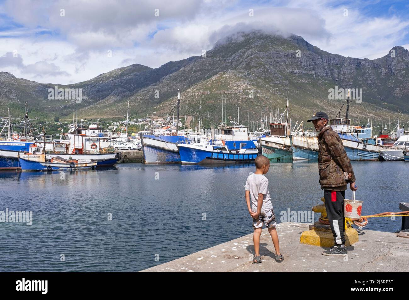 Uomo nero anziano e ragazzo che guarda le barche da pesca nel porto / porto di Hout Bay / Houtbaai vicino a Città del Capo / Kaapstad, Capo Occidentale, Sudafrica Foto Stock