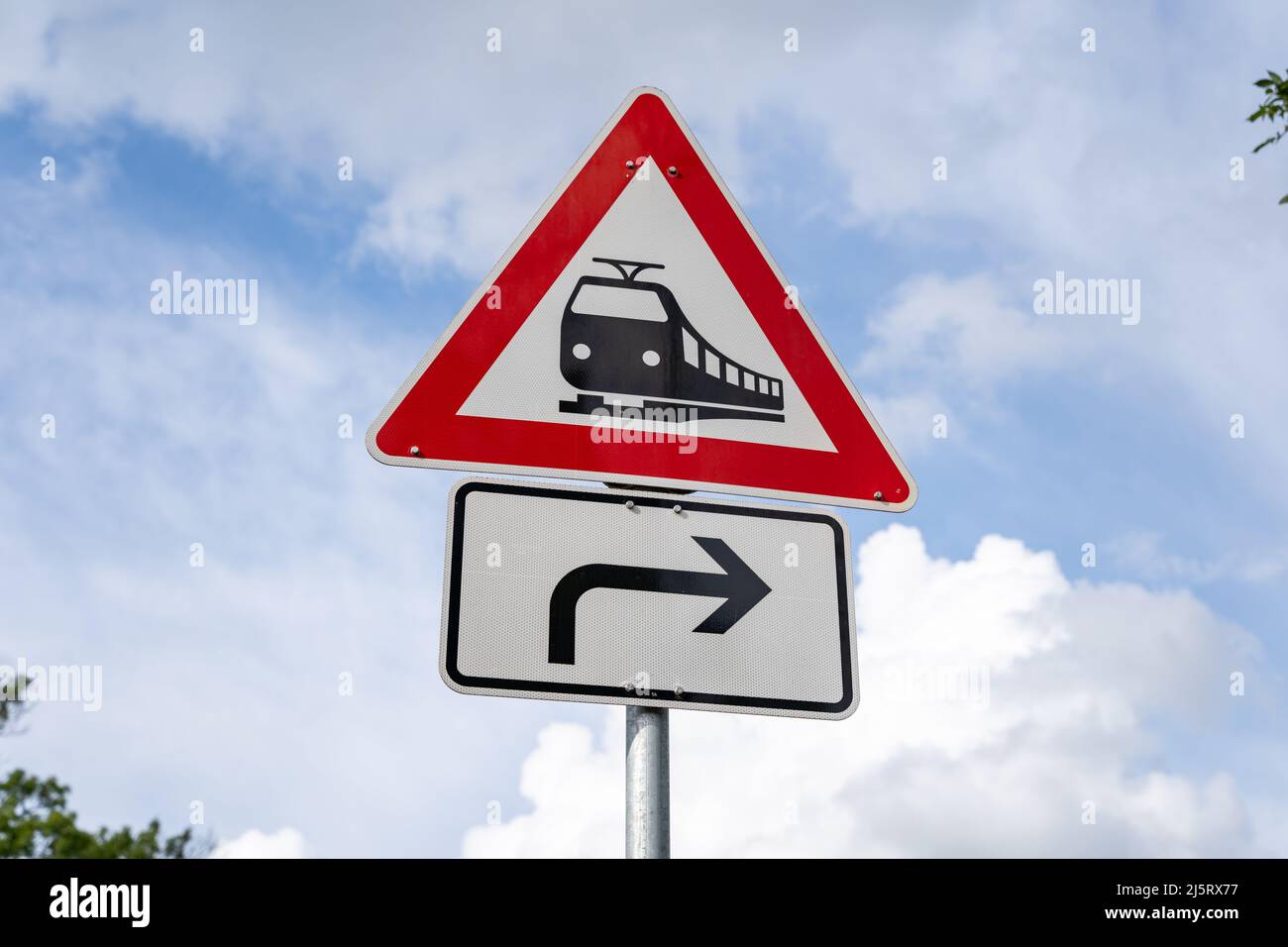 Attraversamento ferroviario senza barriere davanti al cartello stradale in Germania. Simbolo di avvertimento per prestare attenzione davanti al cielo. Un treno nero su un triangolo bianco. Foto Stock