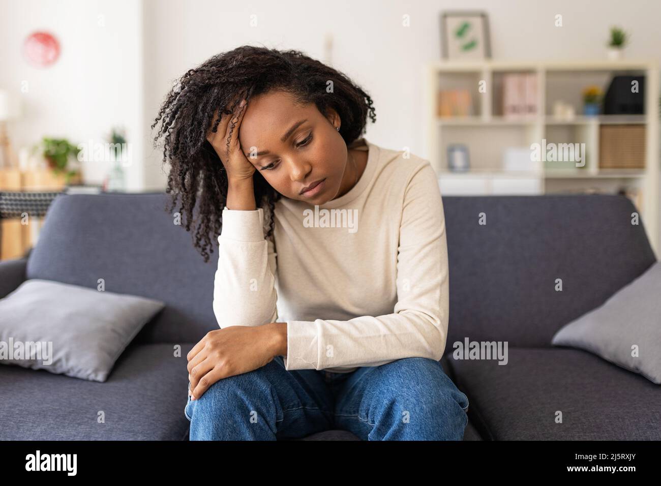 Donna triste pensando ai suoi problemi mentre si siede su un divano a casa Foto Stock