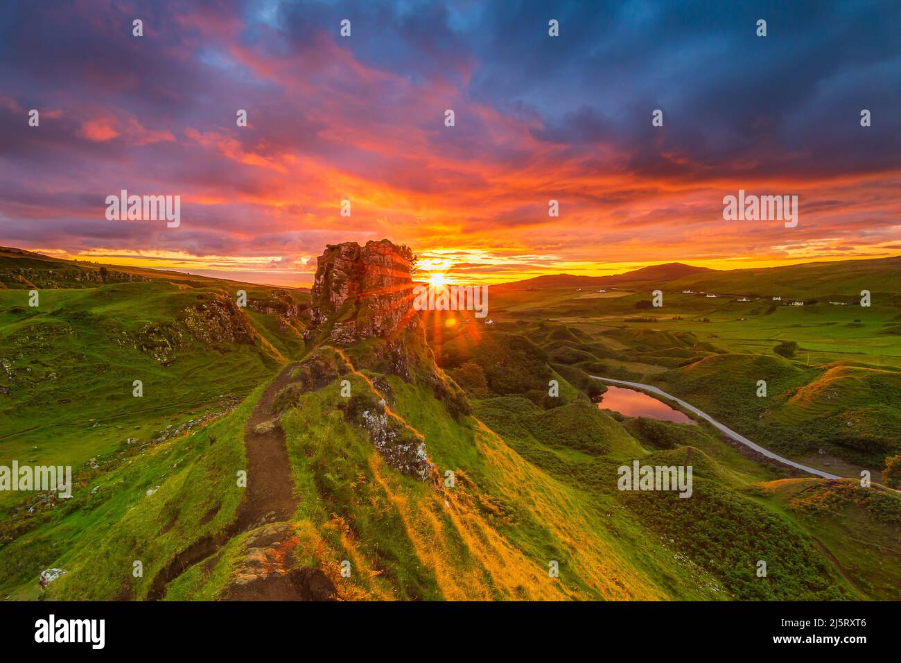 Tramonto con stella del sole in Scozia sull'isola di Skye. Paesaggio con rocce Castello Ewen in estate. Giallo arancio rosso cielo con le nuvole. Strada sabbiosa Foto Stock