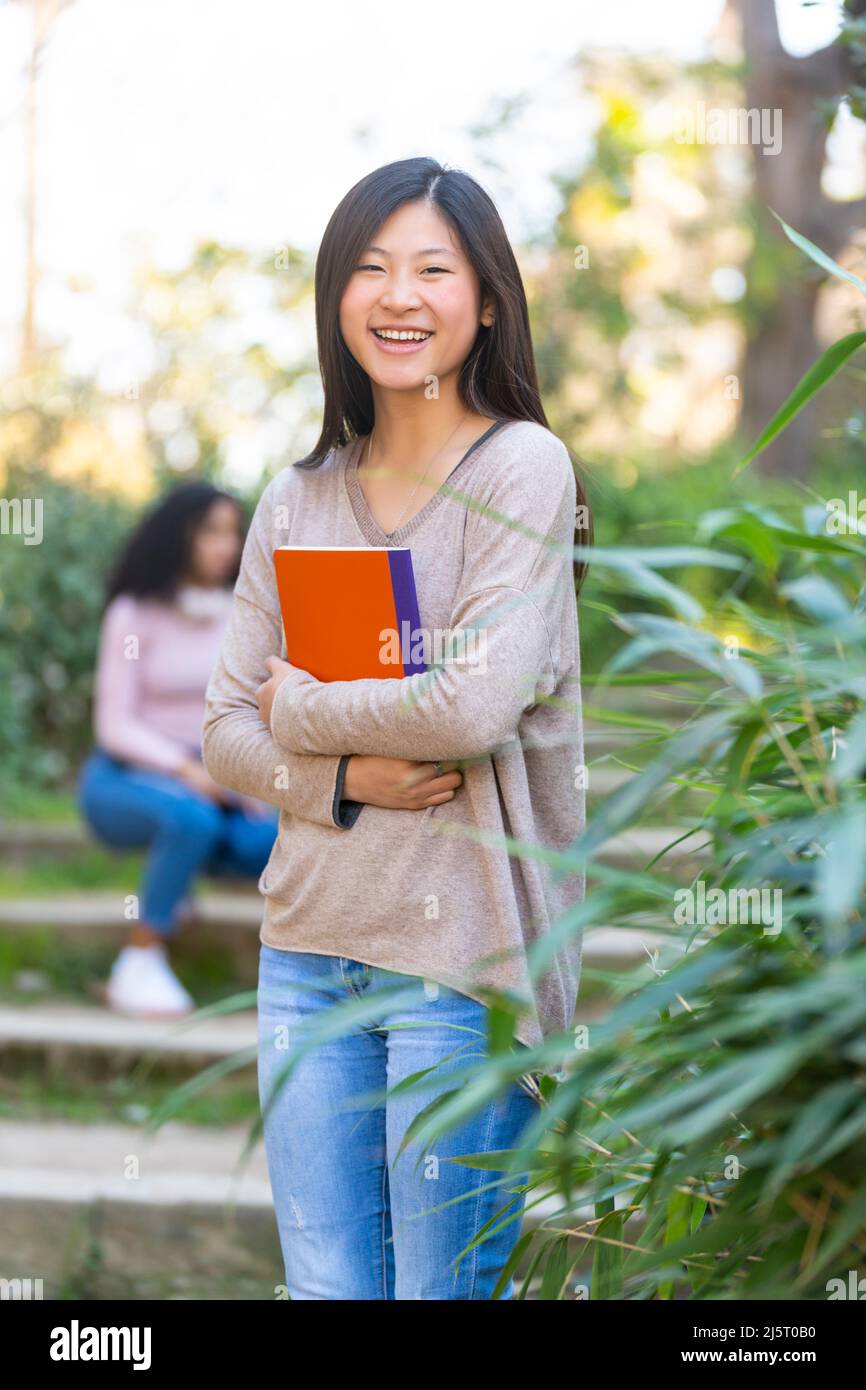 Giovane studentessa asiatica sorridente e che guarda alla macchina fotografica con un notebook Foto Stock