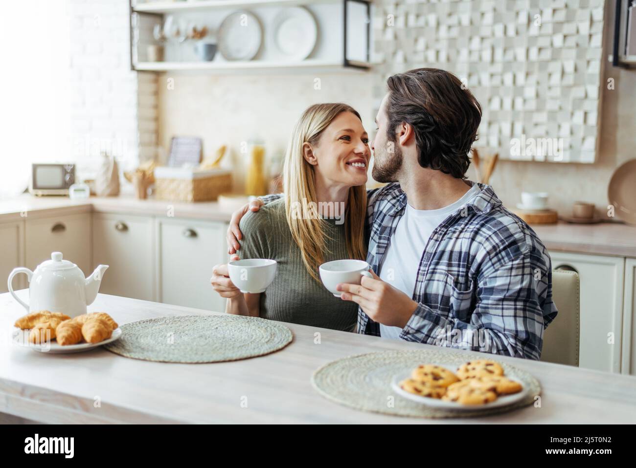 Felice giovane coppia caucasica si guardano, bere tè, godere di tempo libero nel fine settimana in cucina moderna Foto Stock