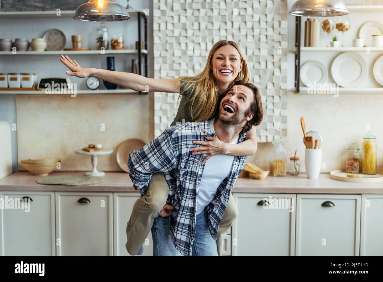 Felice giovane europeo ragazzo rotola sua moglie sul retro e divertirsi insieme in cucina moderna interno in casa propria Foto Stock