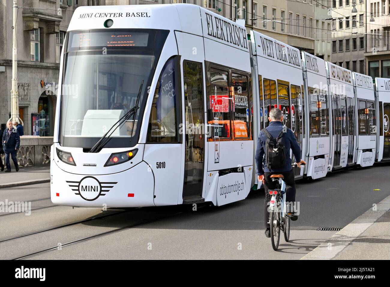 Basilea, Svizzera - Aprile 2022: Il ciclista passa davanti a uno dei moderni tram elettrici della città. La città ha una vasta rete di tram Foto Stock