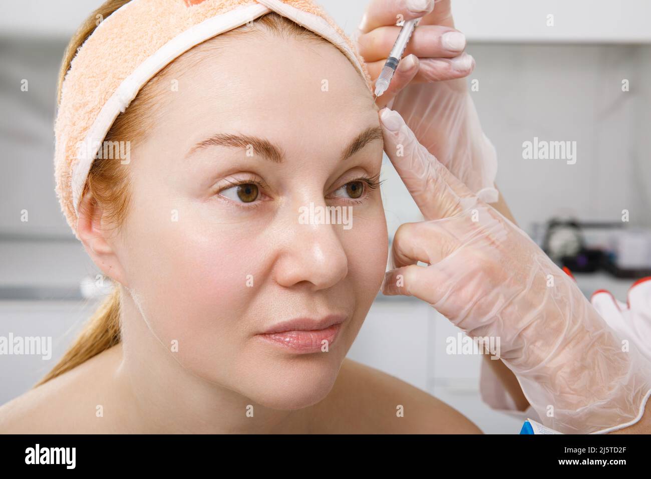 Un cosmetologo esegue una procedura di ringiovanimento delle iniezioni per il viso per stringere e levigare le rughe sulla pelle del viso di una donna Foto Stock