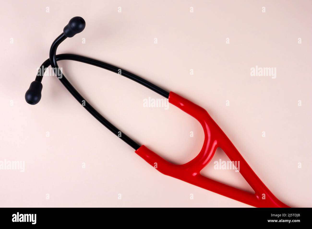 Stetoscopio rosso e nero su sfondo beige. Attrezzatura medica professionale reale. Assistenza sanitaria, controllo, concetto di malattie cardiache. Foto Stock