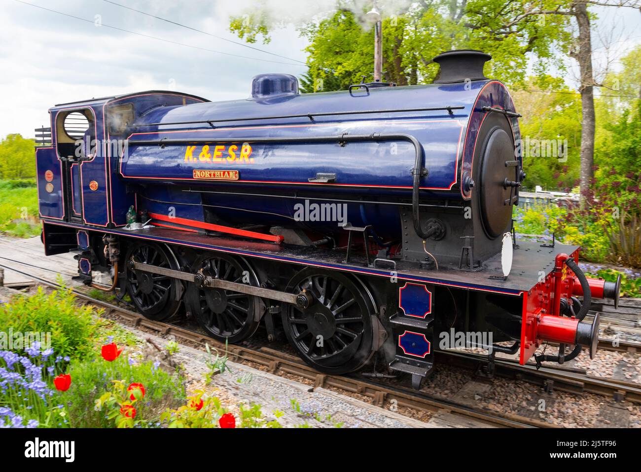 Hunslet austerity 0-6-0ST chiamato Northiam della ferrovia del Sussex del Kent & dell'est alla stazione di Tenterden Town. Paesaggio rurale, di campagna con fiori luminosi Foto Stock