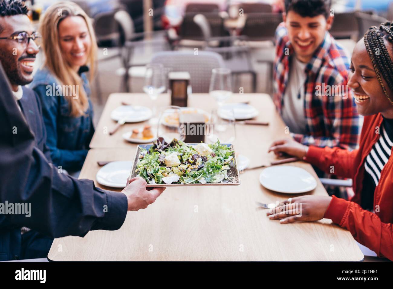 cameriere che serve un'insalata a clienti multietnici su una terrazza ristorante Foto Stock