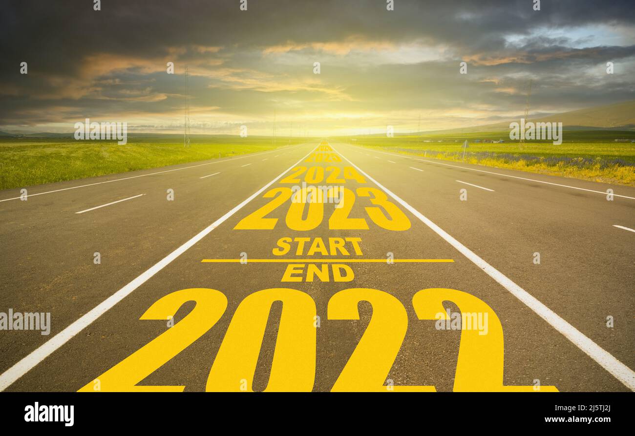 2022 fine e inizio 2023 strada scritta. Anno numero 2023 al tramonto drammatico e su strada vuota. Obiettivo e concetto di visione nel nuovo anno. Foto Stock