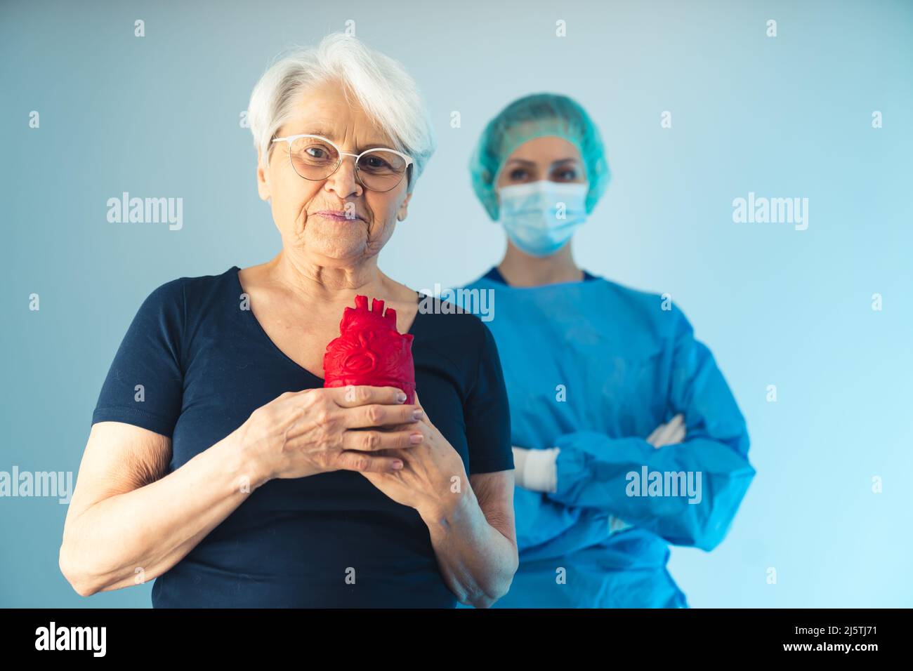 Medico femminile in piedi dietro la donna anziana europea che tiene un rosso cuore artificiale medio colpo studio shot blu sfondo sanitario concetto . Foto di alta qualità Foto Stock